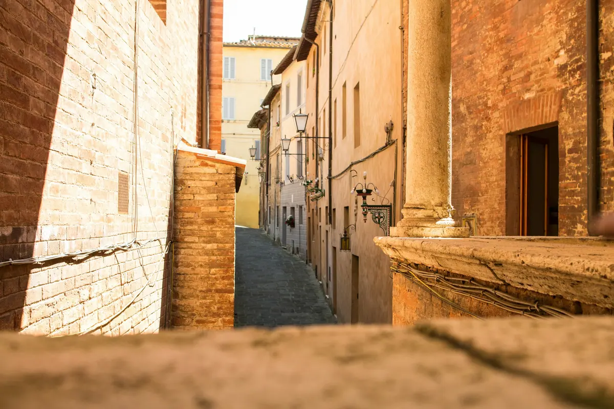 Schmale, sonnige Gasse zwischen alten Backsteinhäusern in einer italienischen Altstadt