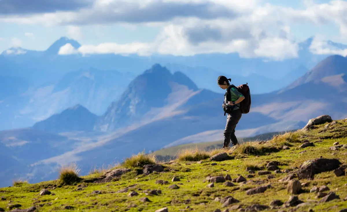 Wanderer mit Rucksack auf einem grasbewachsenen Bergweg vor einer Kulisse aus Alpengipfeln